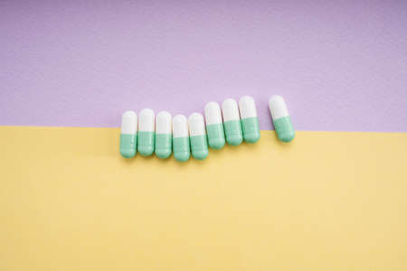 White and light green medicine pill capsule over yellow and purple background.