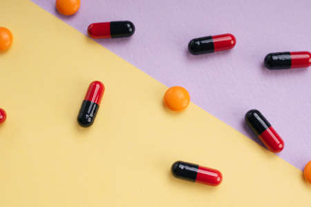 Top view - Red and black medicine pill capsule and orange circle pill over pastel background.の写真素材