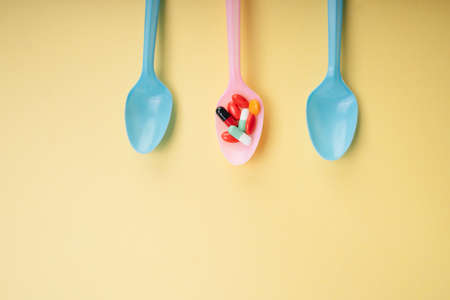 Varity colourful medicine pill capsule on plastic spoon over yellow background.の写真素材