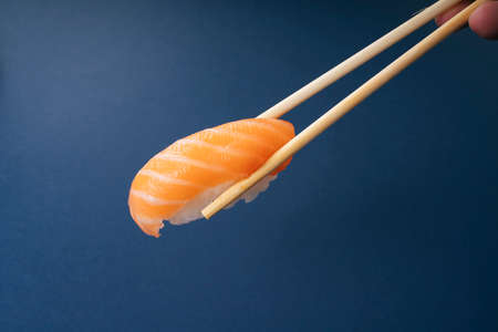Eating fresh salmon sushi with chopstick over blue background.の写真素材