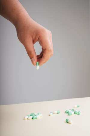 Human hand picking up medicine drug capsule isolate over grey background.の写真素材
