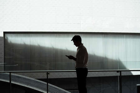 Silhouette view of Mature asian business man on white formal shirt using smartphone outside modern...
