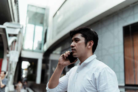 Mature asian business man on white formal shirt using smartphone talking with his friend on the...