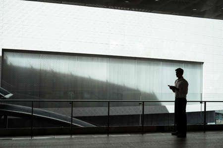 Silhouette view of Mature asian business man on white formal shirt using smartphone outside modern...