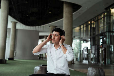 Mature asian business man on white formal shirt feeling happy enjoy music from wireless headset....