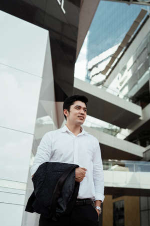 Mature asian business man on white formal shirt holding suit on his arm standing outside the...