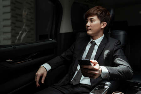 Young asian businessman on black suit using smartphone in a car.の写真素材
