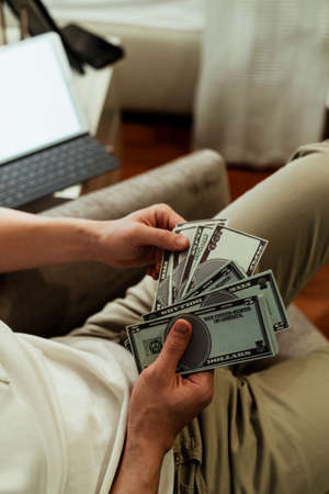 Close up of rich man counting banknote sitting on a couch at home. Hand counting money bank.の写真素材
