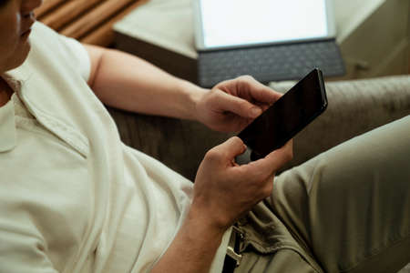 Close up hand of asian guy using smartphone sitting on a couch.の写真素材