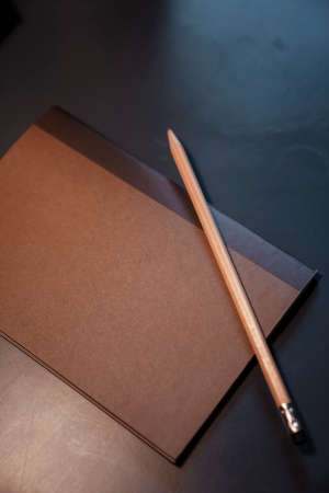 Top view - Brown book and pencil on black working desk.