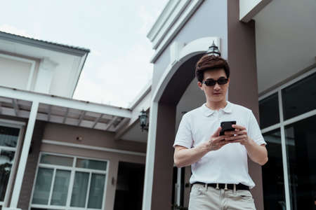 Rich business asian man wearing sunglasses holding smartphone walking outside resort.の写真素材