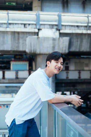 Teenager guy with bright smile standing at the balcony of the building with skytrain's station as a background.の写真素材
