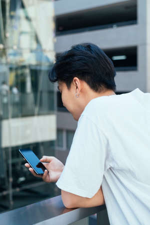 Back shot of teenage guy bend down on glasses barricade while use his mobile phone.の写真素材