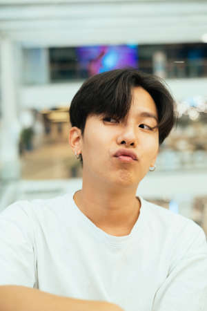 Teenage guy in white t-shirt making a duck face while waiting for his friend in the mall.の写真素材