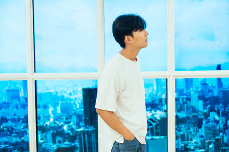 Teenage guy in jeans and white t-shirt standing next to the glasses window on high building.の写真素材