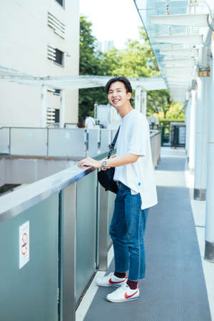 Black hair teenage guy standing at the terrace with bright smile at the glasses building.