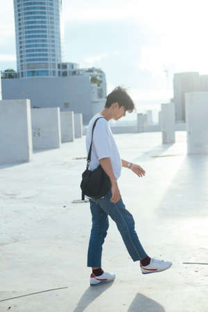 Teenage guy in jeans and white t-shirt standing in the walking alone on the rooftoop of high...