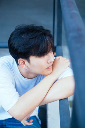 High angle shot of teenage guy in white t-shirt rest his head and arms on the handrail and look at...