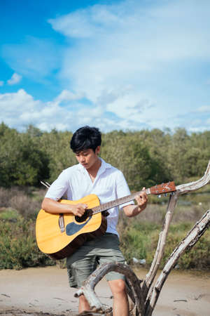 A musician guy sitting on a log among the dry forest playing his beloved guitar.の写真素材