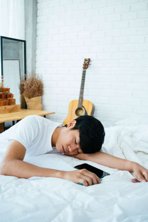 Black hair guy fall asleep while write the letter on the white bed in his bedroom.