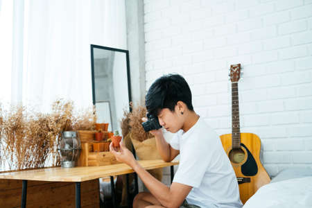 A man in white t-shirt taking a photo of his small cactus in a pot with his camera.