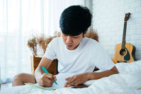 Black hair guy write the letter on the white bed in his bedroom.の写真素材