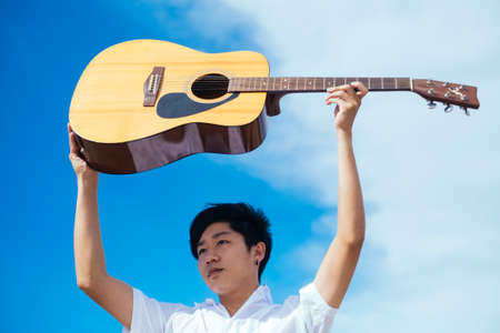 Black hair guy raise the guitar over his head to the blue sky.