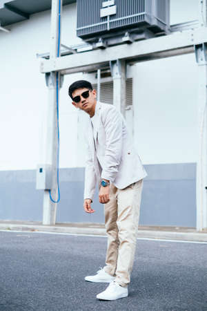A man in white suit wearing sunglasses standing like a hunchback next to the factory.の写真素材