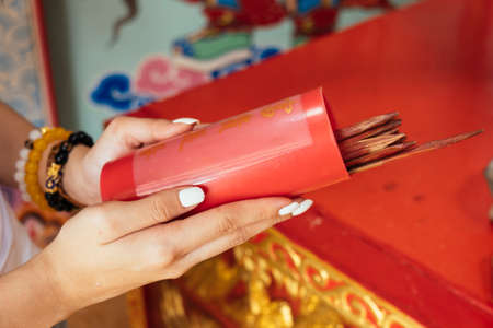 Cropped image of wooden red cylinder contain fortune stick in woman's hands.