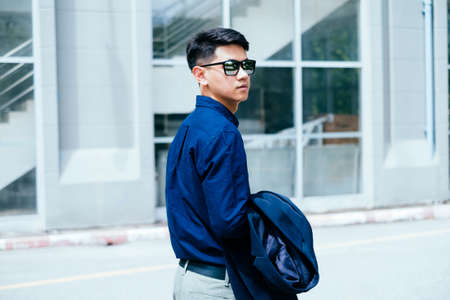 A man in dark blue shirt walking pass by the glasses building in sunlight summer.