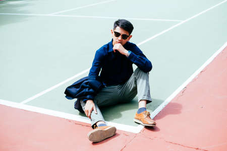 A man in dark blue shirt and sunglasses sitting in the sunlight at the tennis court.