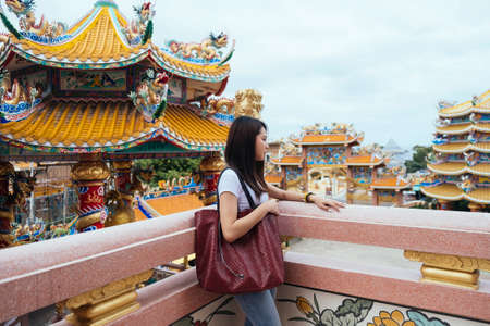 Long hair woman in casual clothes standing at the terrace of temple with red big bag.