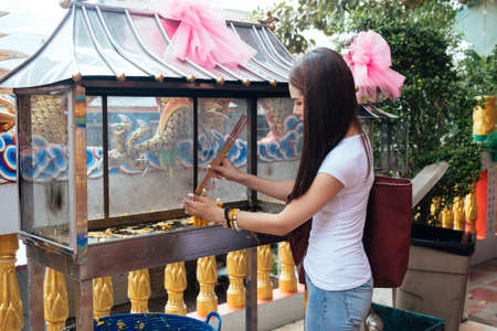 Long hair woman in casual clothes try to burn joss stick with the candle.