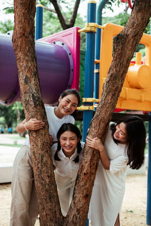 Triple twin sister play together around the tree like V sign with happiness in the playground.の写真素材