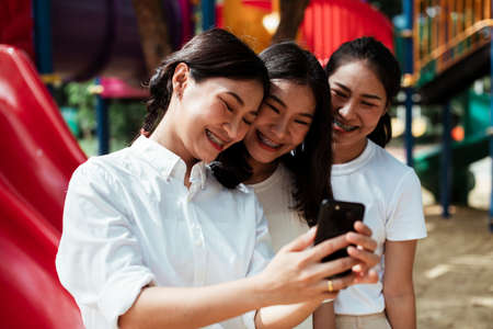 Triple twin sister take a selfie at the end of red slider in the playground of the park.の写真素材