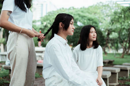 Triple twin sister are in the park, one of them make a pigtails hair for another one.の写真素材