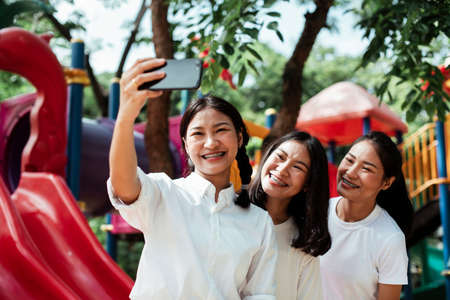 Triple twin sister take a selfie at the end of red slider in the playground of the park.の写真素材