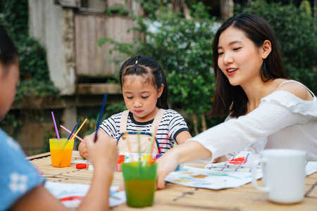 Asian big sister helping little sister painting water colour on paper outdoors.の写真素材