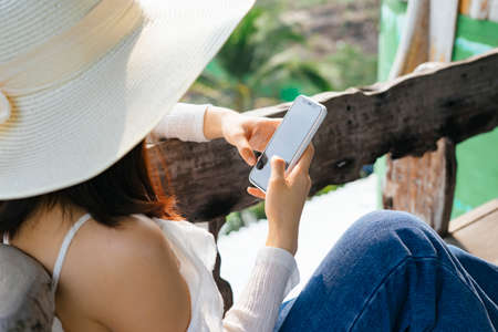 Close up hands of asian woman on white shirt using smartphone on bench at countryside farm.の写真素材