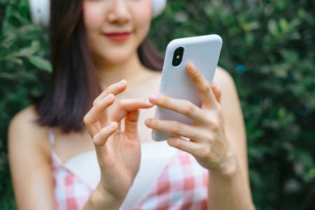 Close up hand pretty girl touching on smartphone standing at green tree plant wall.の写真素材