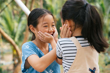 Playful little asian girl touching face to face in nature. Sisters enjoy playing together at farm. Traveling in nature. Countryside area.の写真素材
