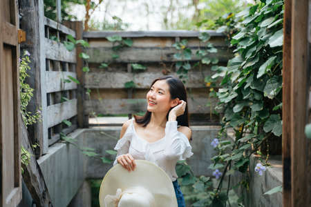 Thai asian young woman on sexy white dress holding hat at countryside abandon garden.の写真素材