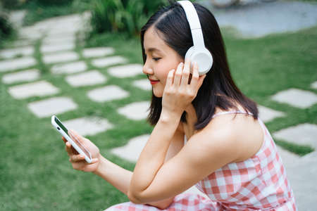 Sideview of Beautiful young woman in headphones listening to music smiling with closed eyes sitting in garden.の写真素材
