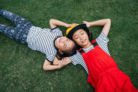 Two sister asian little girls laying on grass field with happiness. Sleeping on meadow grass field.の写真素材