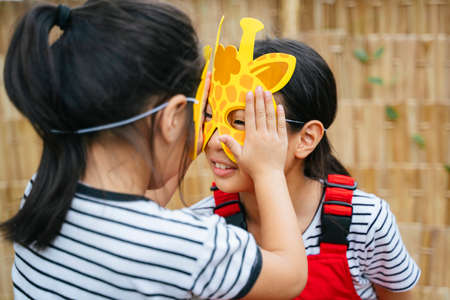 Two asian little girl wearing animal mask playing together, touching face, stop biting me.の写真素材