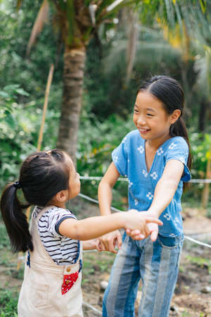 Two asian little girl holding hands having fun at farm in country district. Travel in nature.の写真素材