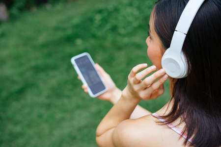 Shoulder top view - Asina girl listen to music with white wireless headphone, holding smartphone to control music platform.の写真素材