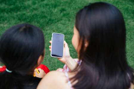 Over shoulder back view - Smartphone screen on woman hand playing together at green field.