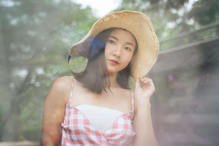 Beautiful young asian woman on pink dress wearing big hat travel in nature. Eco traveling. standing behind steam.の写真素材
