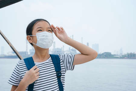 Virus protection concept - asian little girl wearing protective mask, standing near river in smog...